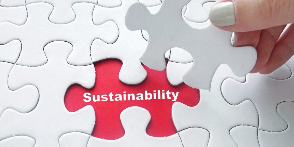 Close up of girl's hand placing the last jigsaw puzzle piece with word Sustainability as business concept